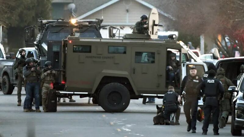 Law enforcement officers aim their weapons at a home during a standoff in Grants Pass, Ore.,...