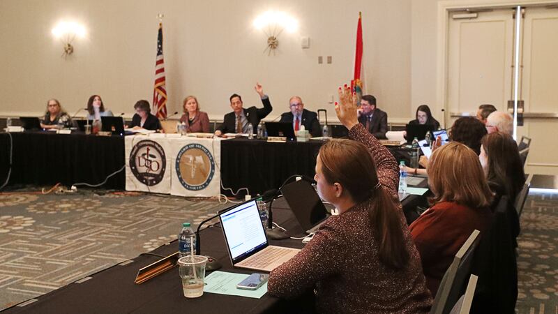 Members raise their hands during a vote in a joint board meeting of the Florida Board of...
