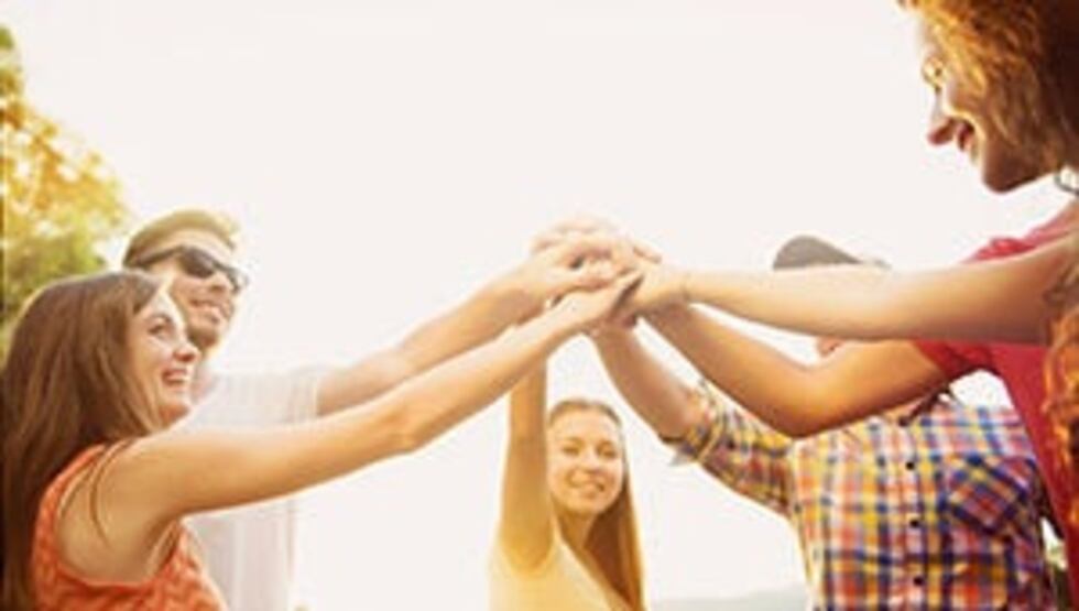 A small group of people holding their hands in the middle, while they are standing in a circle.